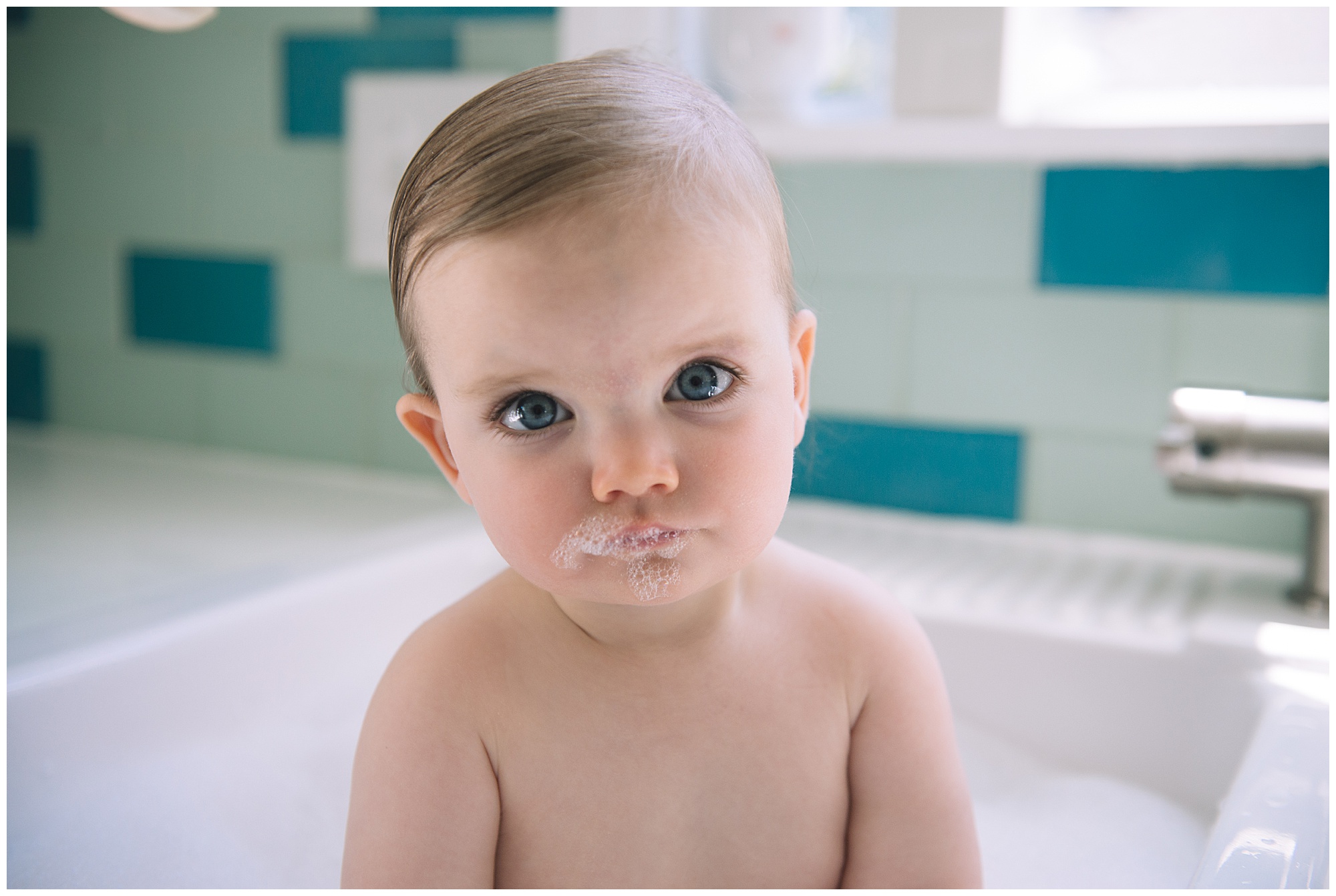 Baby in kitchen sink bath with bubbles on mouth and big blue eyes Emily Ann Photography Seattle Family and Newborn Photographer.