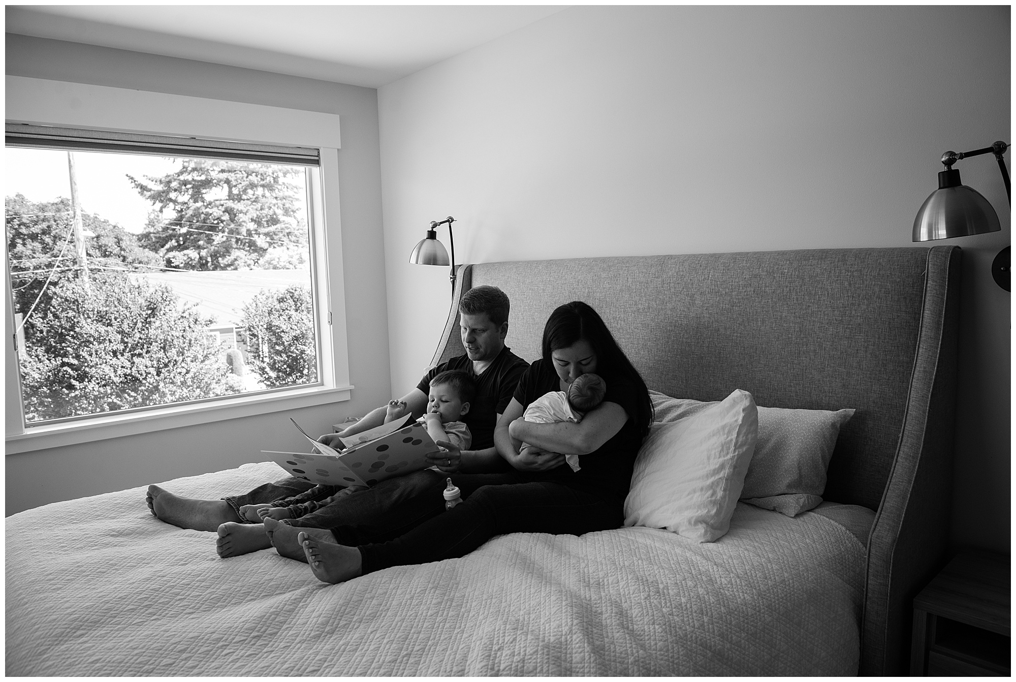 Black and White Newborn Lifestyle photo of family reading on bed Emily Ann Photography Seattle