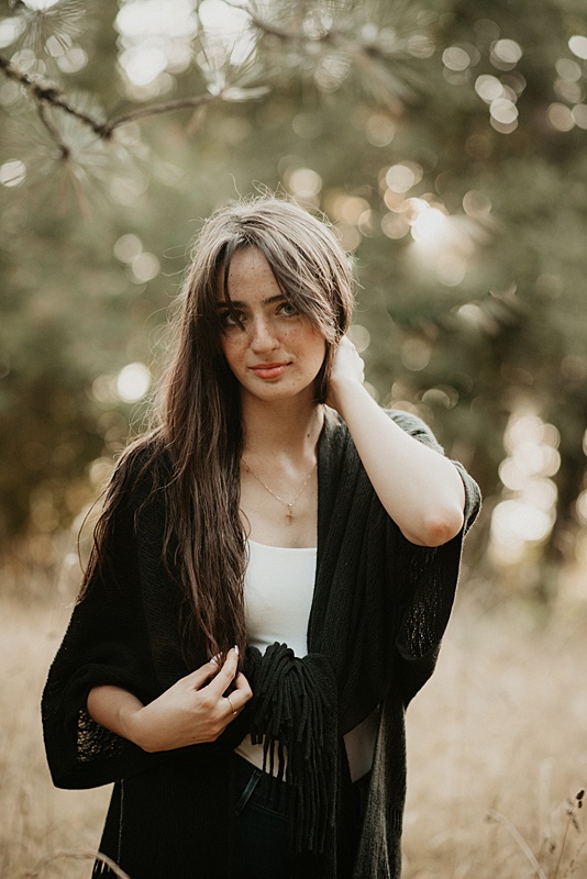 High school senior girl looking at camera with beautiful bokah in trees behind her.