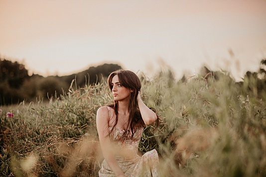 high school senior girl sitting in tall field of green grass