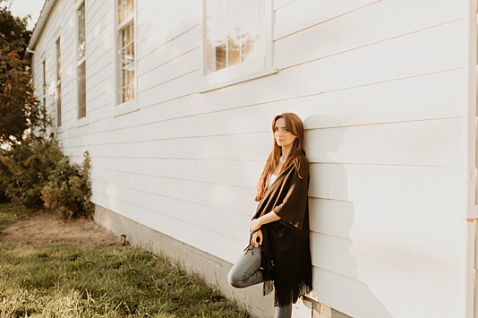 High school senior girl leaning up against white building during sunset at Discovery Park