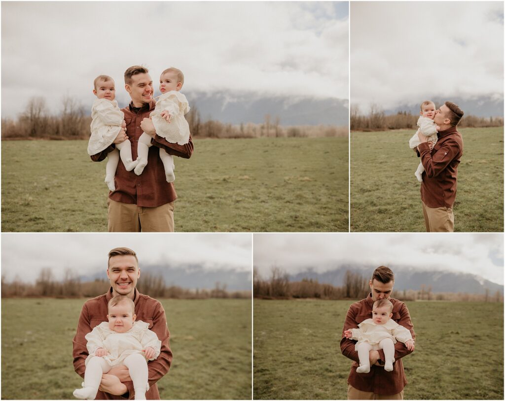 Dad holds baby twin girls dressed in matching white dresses. Family photos in North Bend, WA with foggy Mount Si in the background.