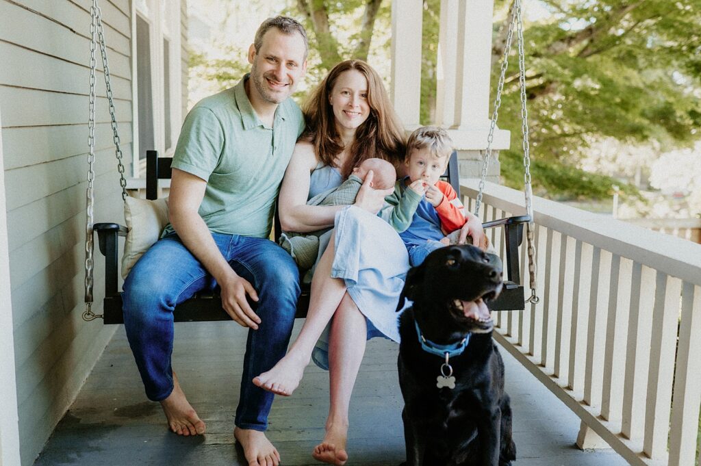Mom, dad, big brother, new baby and black lab sitting on porch swing in Seattle
