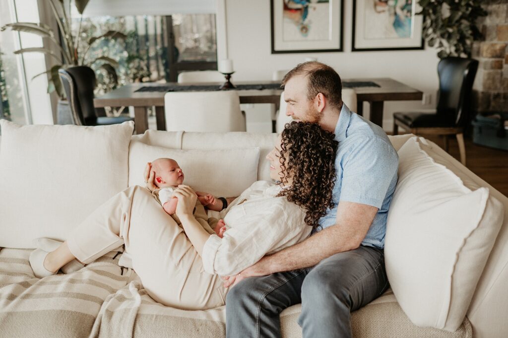 mom and dad cuddling newborn baby boy on cream couch in light filled home in seattle, wa